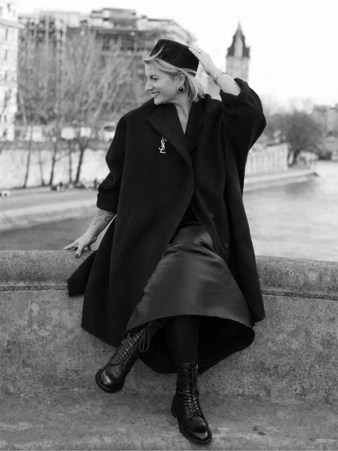 Woman in black coat sitting outdoors in city park, stylish fashion, urban scenery.
