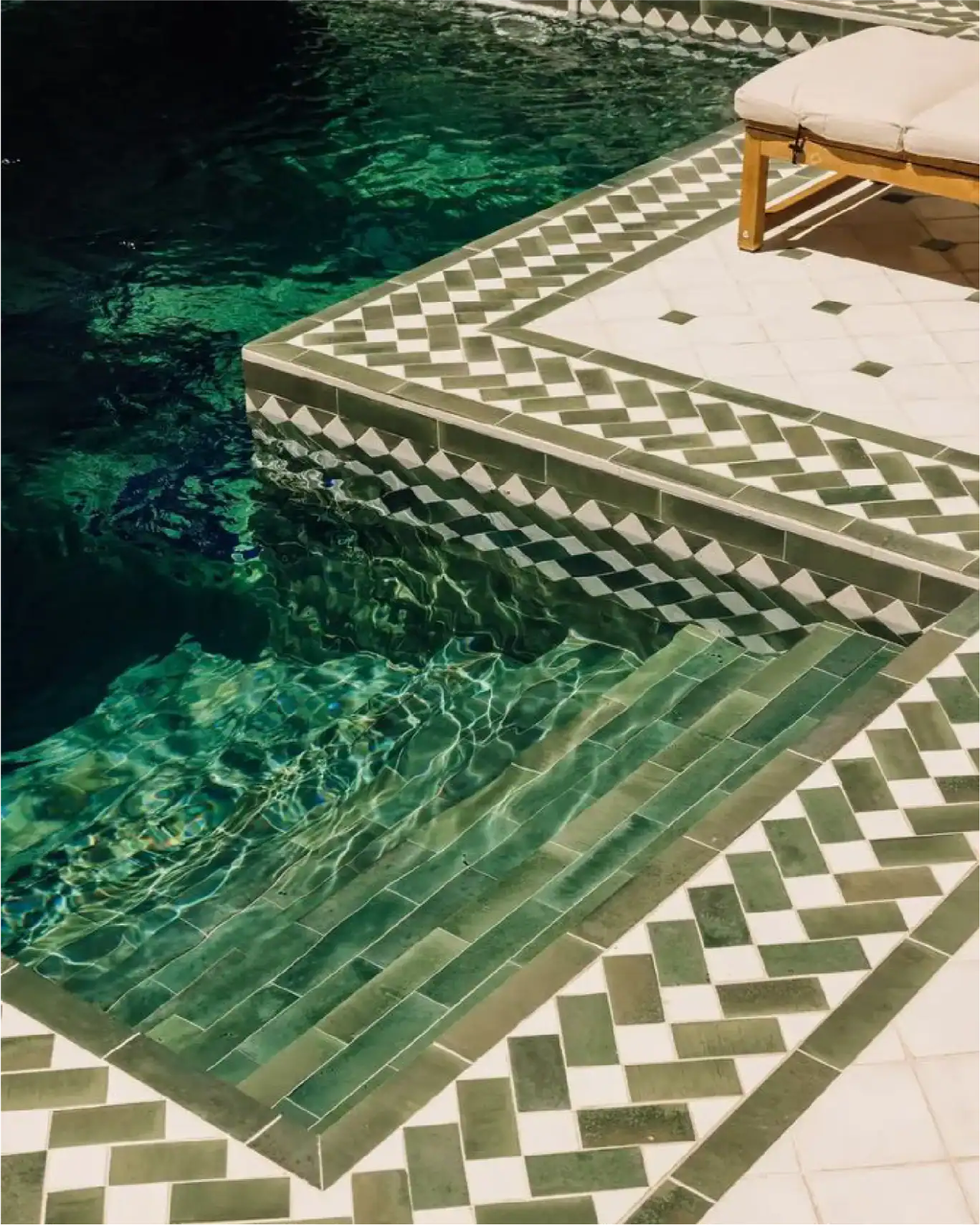 Gradini piastrellati e zona lounge a bordo piscina con pavimentazione a motivo geometrico.