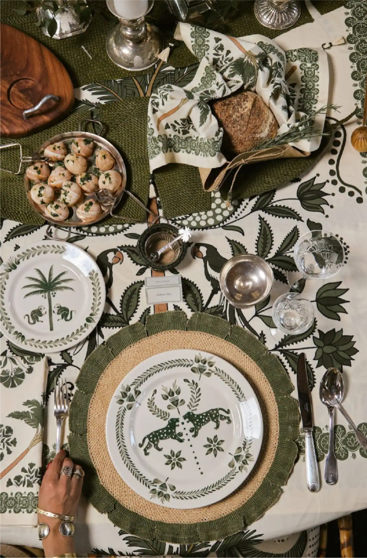Impostazione della tavola a tema tropicale con piatti decorativi, biscotti e vegetazione lussureggiante.