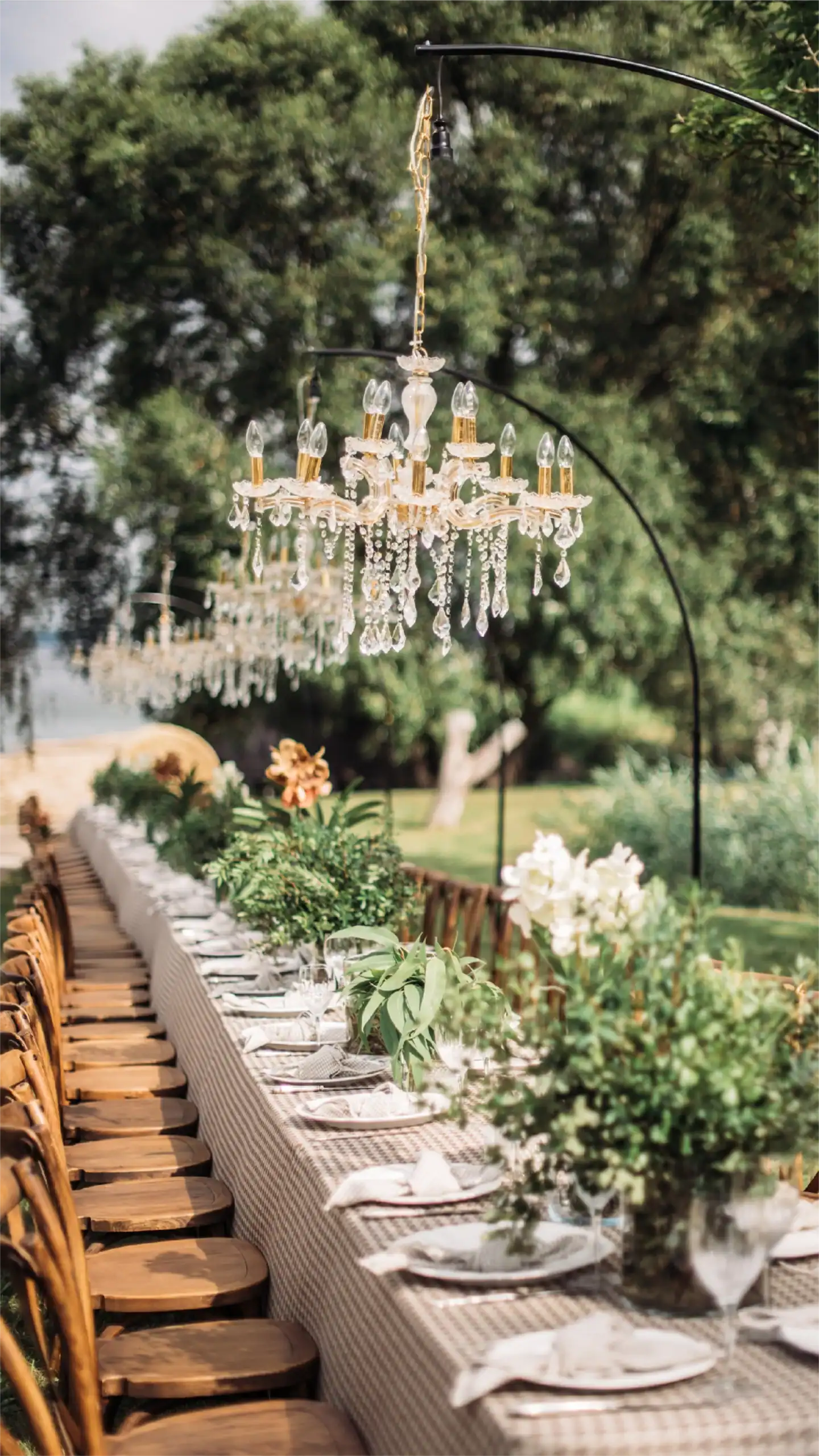 Tavolo da pranzo all'aperto con lampadario, piante lussureggianti e ambientazione in giardino.