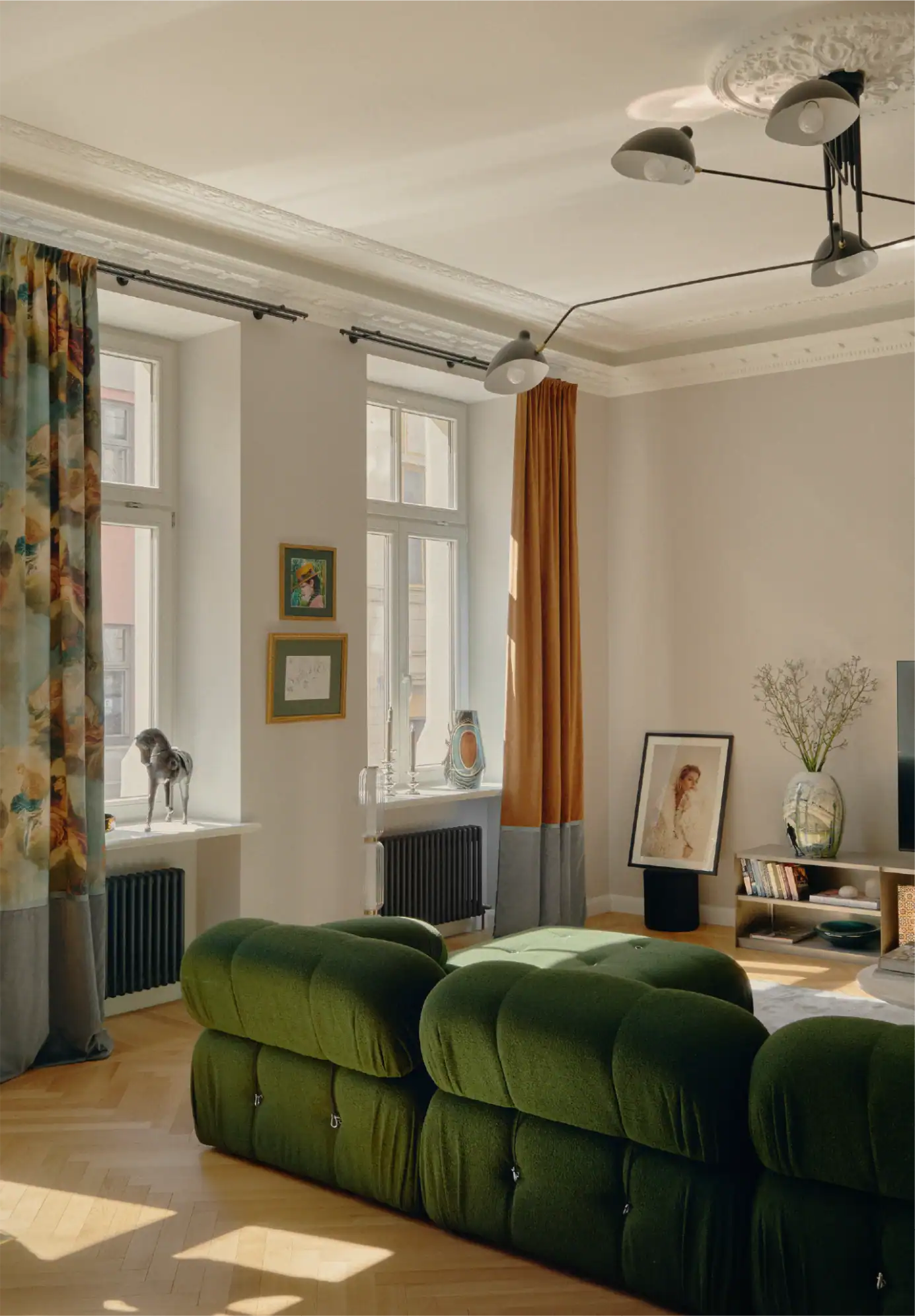 Soggiorno luminoso con divano in velluto verde, luce naturale ed elementi decorativi.